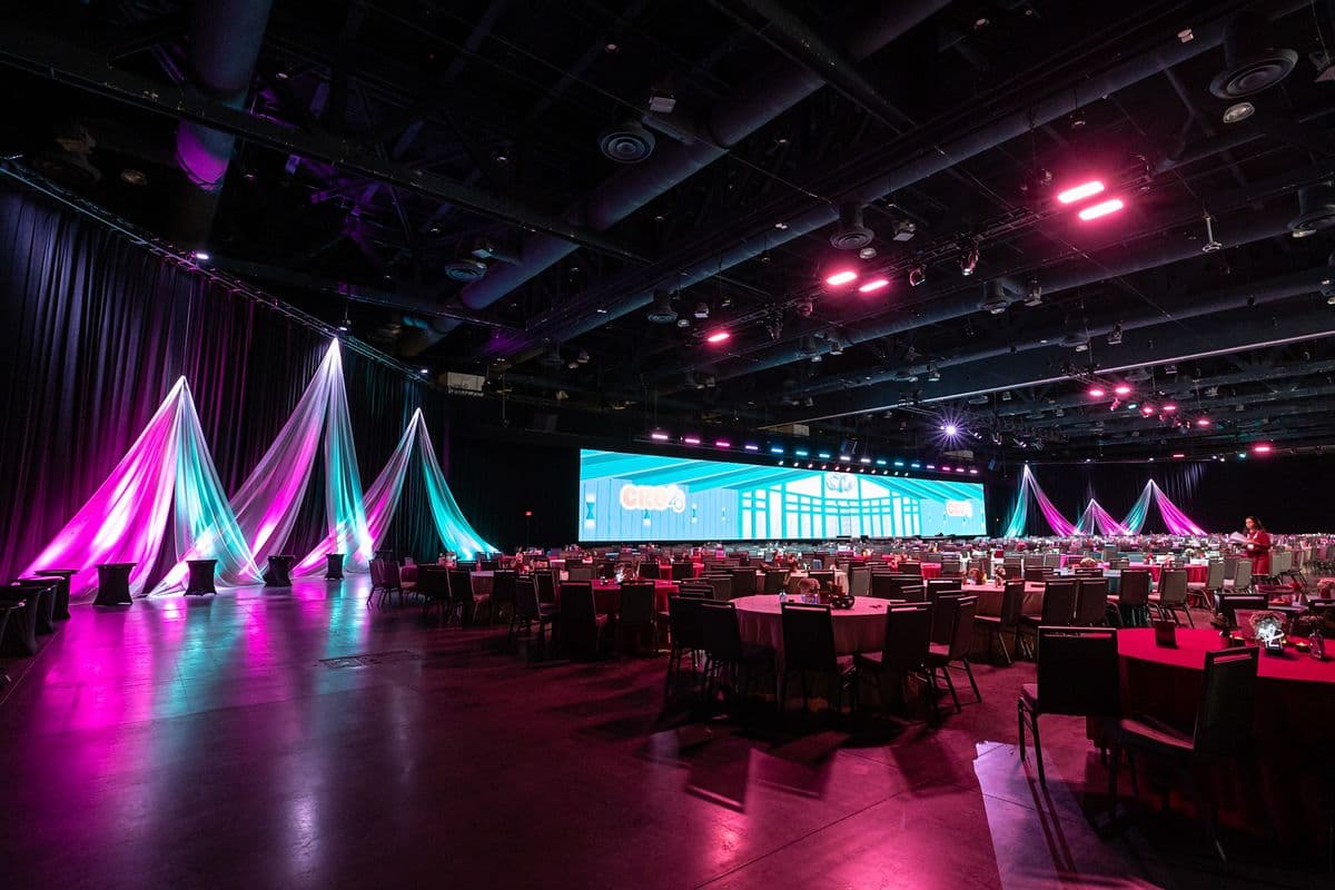 Corporate general session room lit in teal and magenta with suspended drape