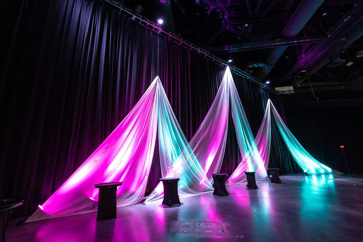 Suspended drape panels lit in magenta and teal on a ballroom floor